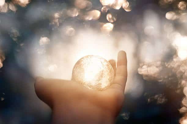 unrecognizable witch hand holding magic globe, defocused lights in background.